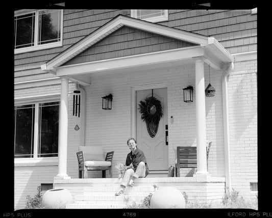 Person sitting on front porch steps of a house.