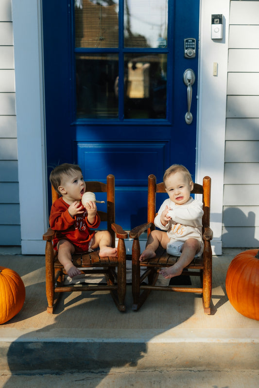 Two babies sitting on rocking chairs on porch