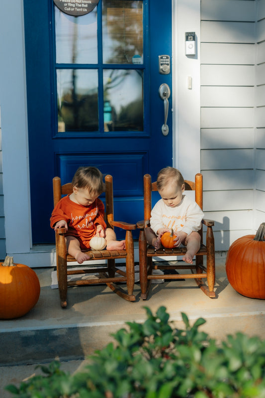 Two babies sitting in rocking chairs with pumpkins