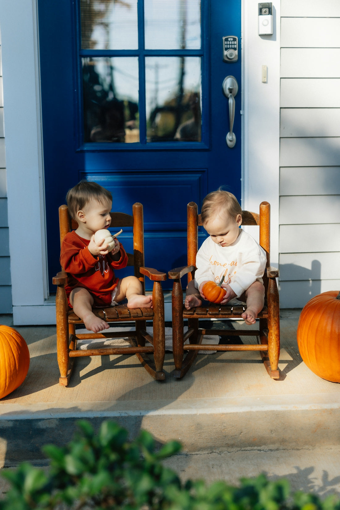 Two babies sitting on rocking chairs with pumpkins.