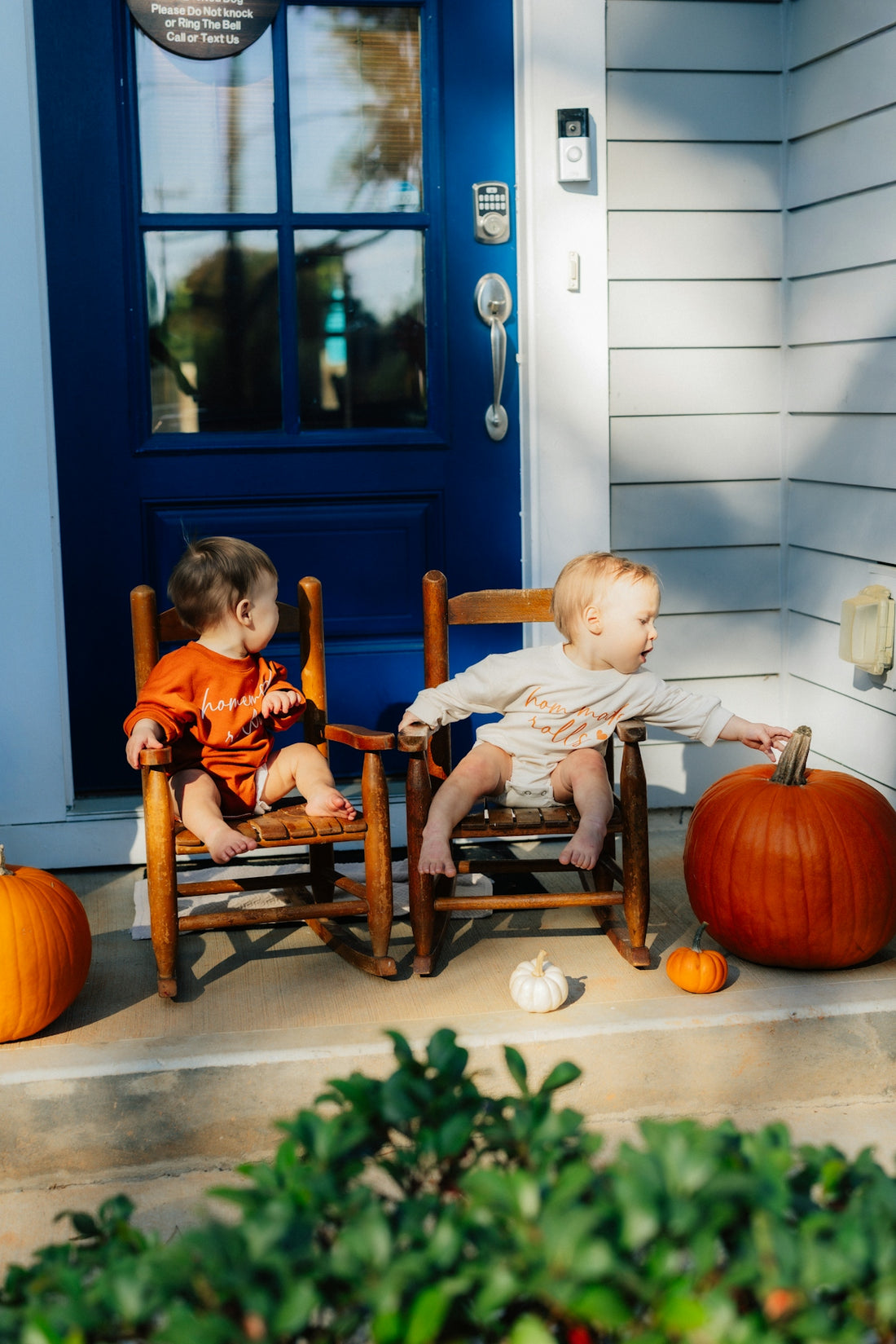 Two babies sit on rocking chairs with pumpkins.