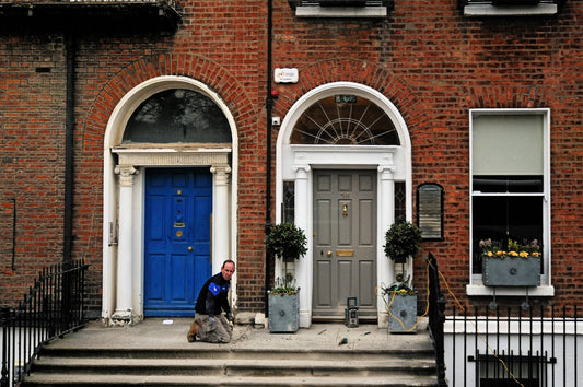 Man cleaning steps in front of brick building with doors.