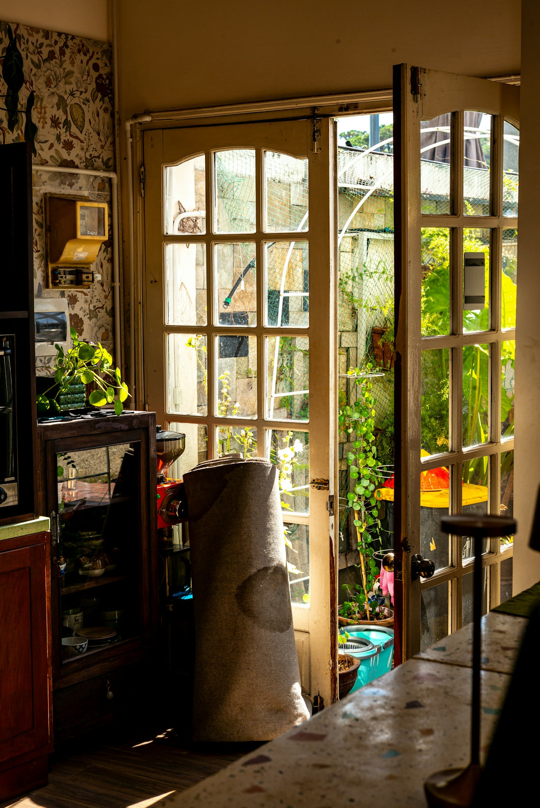 Sunlight streams through glass doors into a cluttered room.
