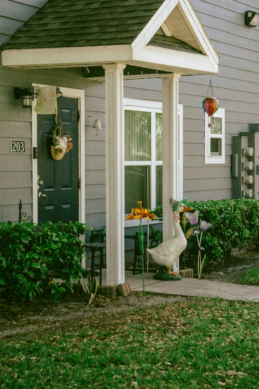 A goose statue stands by a decorated doorway with pumpkins.