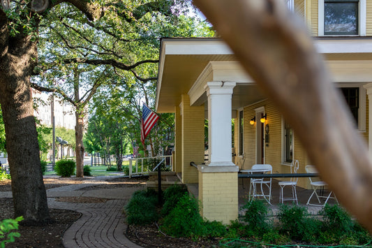 Yellow house with a porch, american flag, and brick pathway.