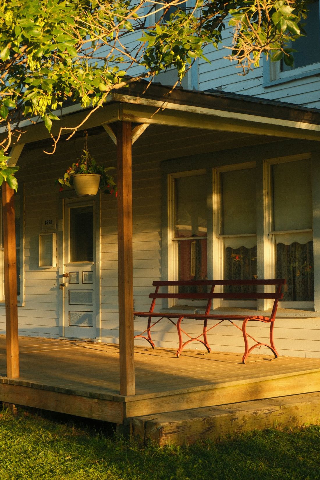 A red bench sits on a sunlit house porch