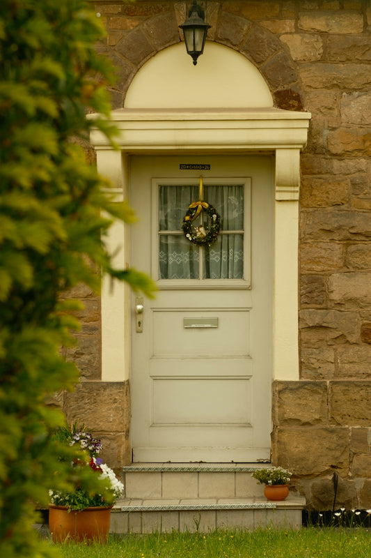 Light front door with a wreath on a stone building.