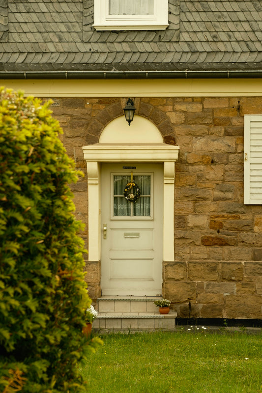 Light front door on a stone house with green shrub.