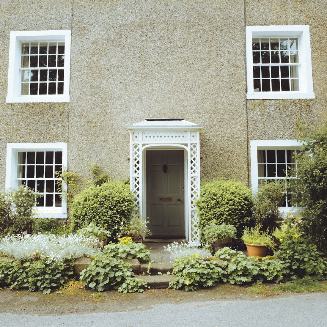 Charming house with white windows, ornate porch, and green garden.