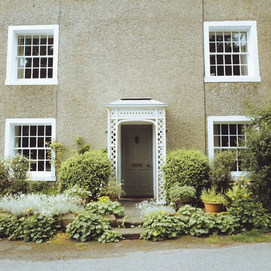 Charming house with white windows, ornate porch, and green garden.