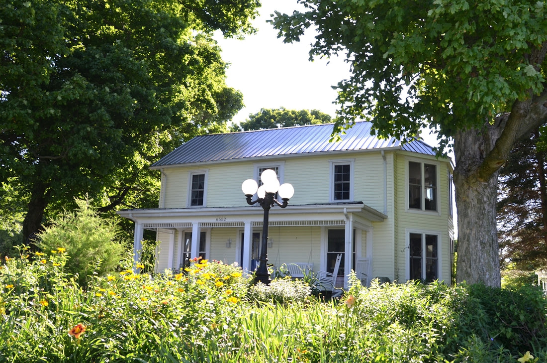 Historic house with a porch and lamp amidst green foliage.