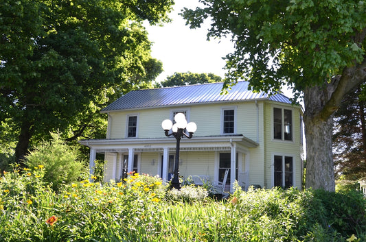Historic house with a porch and lamp amidst green foliage.