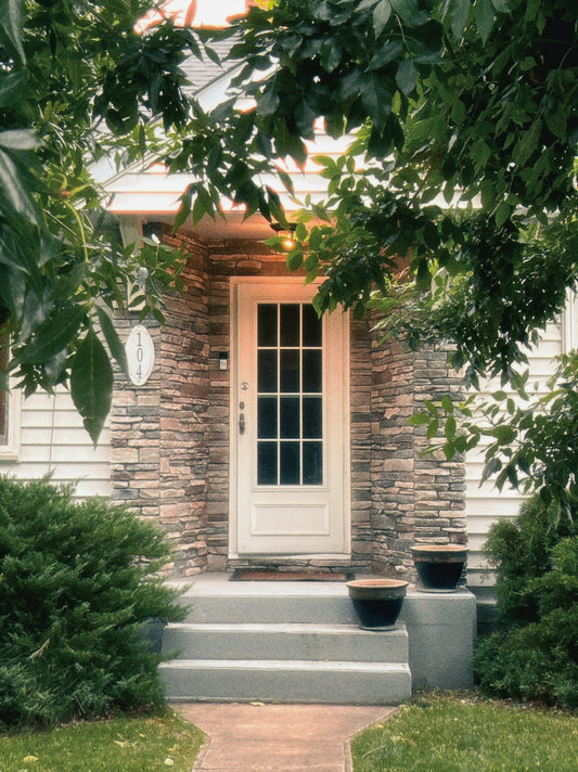 A white front door with stone siding and green foliage.