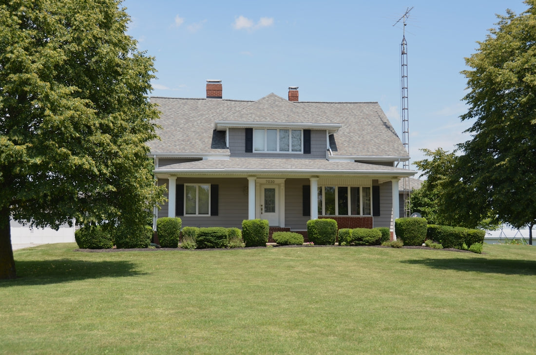 Traditional grey house with a porch, green lawn, and trees.