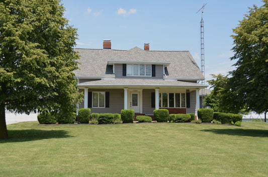 Traditional grey house with a porch, green lawn, and trees.
