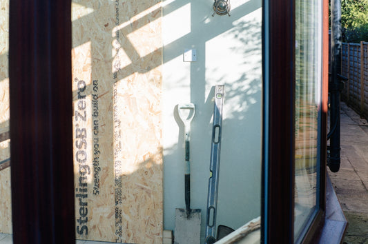 Shovel and tools leaning against osb wall in sunlight