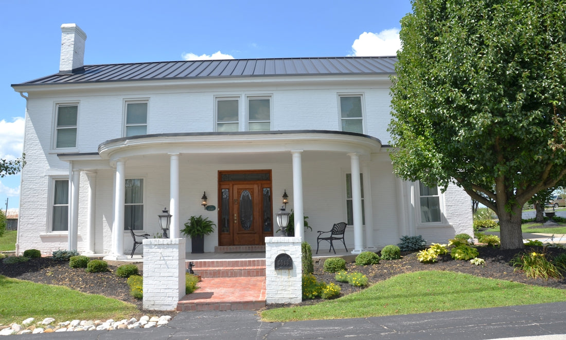 A white brick house with a curved porch and dark metal roof