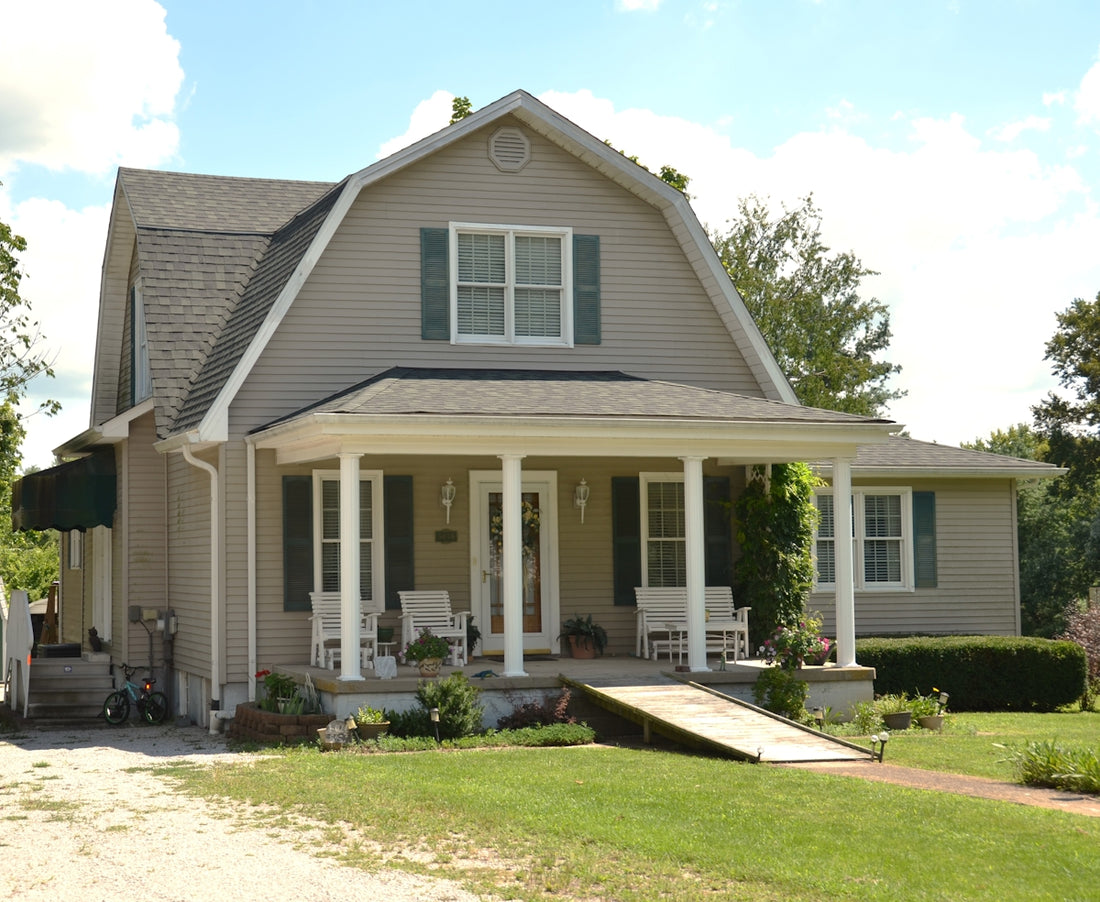 A beige house with a gambrel roof and a front porch with white columns