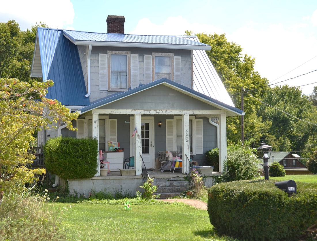 A grey house with a blue metal roof and a covered front porch